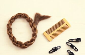 Longue tresse de cheveux bruns posée sur une table en bois clair à côté d'un peigne en bois et de pinces de coiffure noires