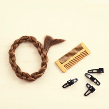 Longue tresse de cheveux bruns posée sur une table en bois clair à côté d'un peigne en bois et de pinces de coiffure noires